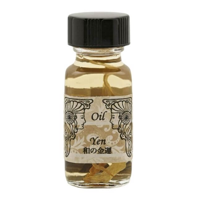 「オイル イェン」と書かれた黒いキャップの付いた小さなガラス瓶には、透明な液体と小さな浮遊葉が入っています。ラベルには、女神のような女性の横顔の鏡絵が描かれており、このブレンドが絶妙なメモリー オイルであることを示唆しています。
